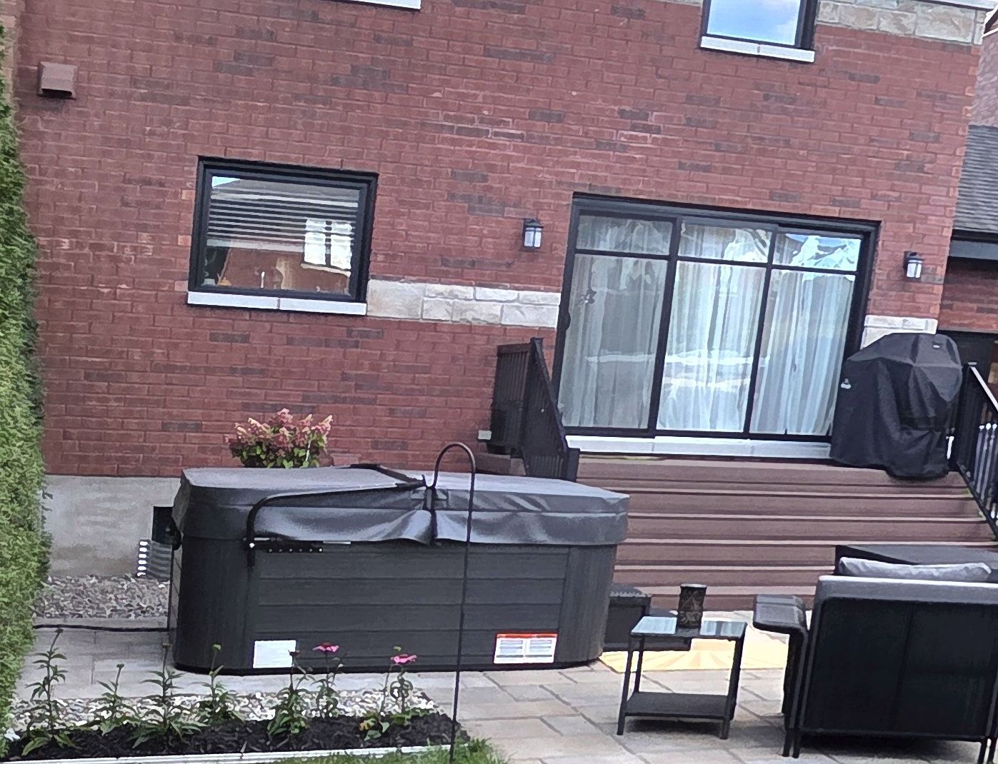 Une terrasse arrière avec un jacuzzi couvert, un escalier en bois menant à une maison en briques et du mobilier de jardin.