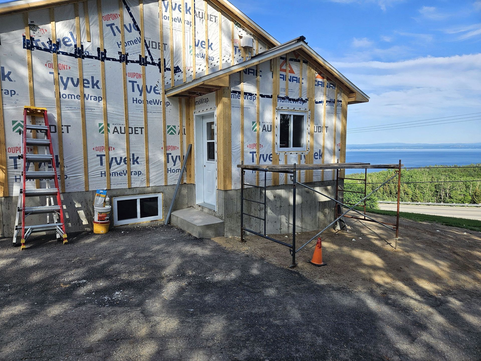 Extérieur inachevé d'une maison en bois en construction, avec pare-vapeur Tyvek, échelle, échafaudage et vue sur la mer.