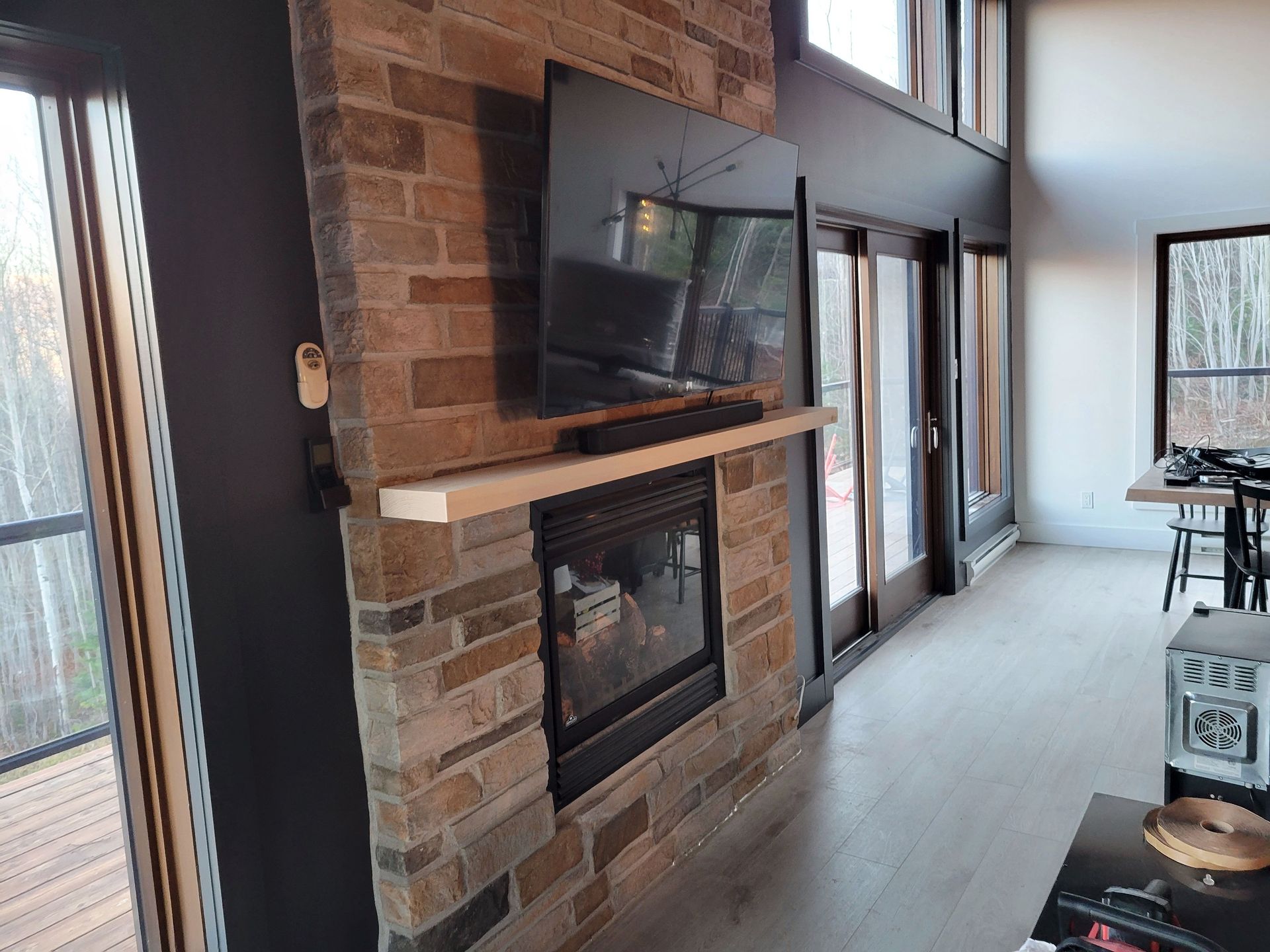 Une cheminée en pierre avec un téléviseur mural et un manteau de cheminée en bois dans une pièce moderne avec de grandes fenêtres.