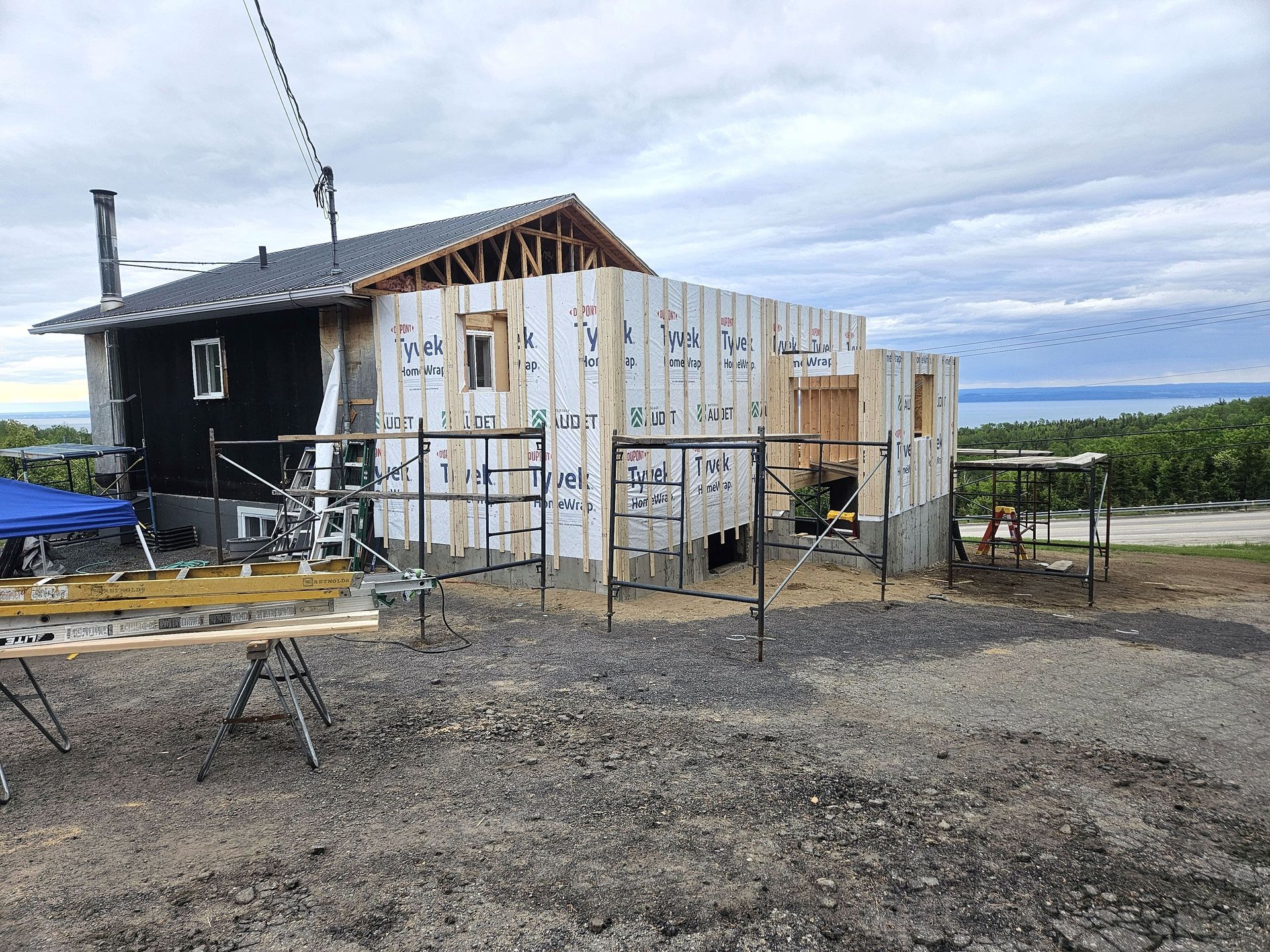 Une vieille cabane en cours de rénovation, avec un nouveau revêtement extérieur blanc résistant aux intempéries et des échafaudages tout autour.
