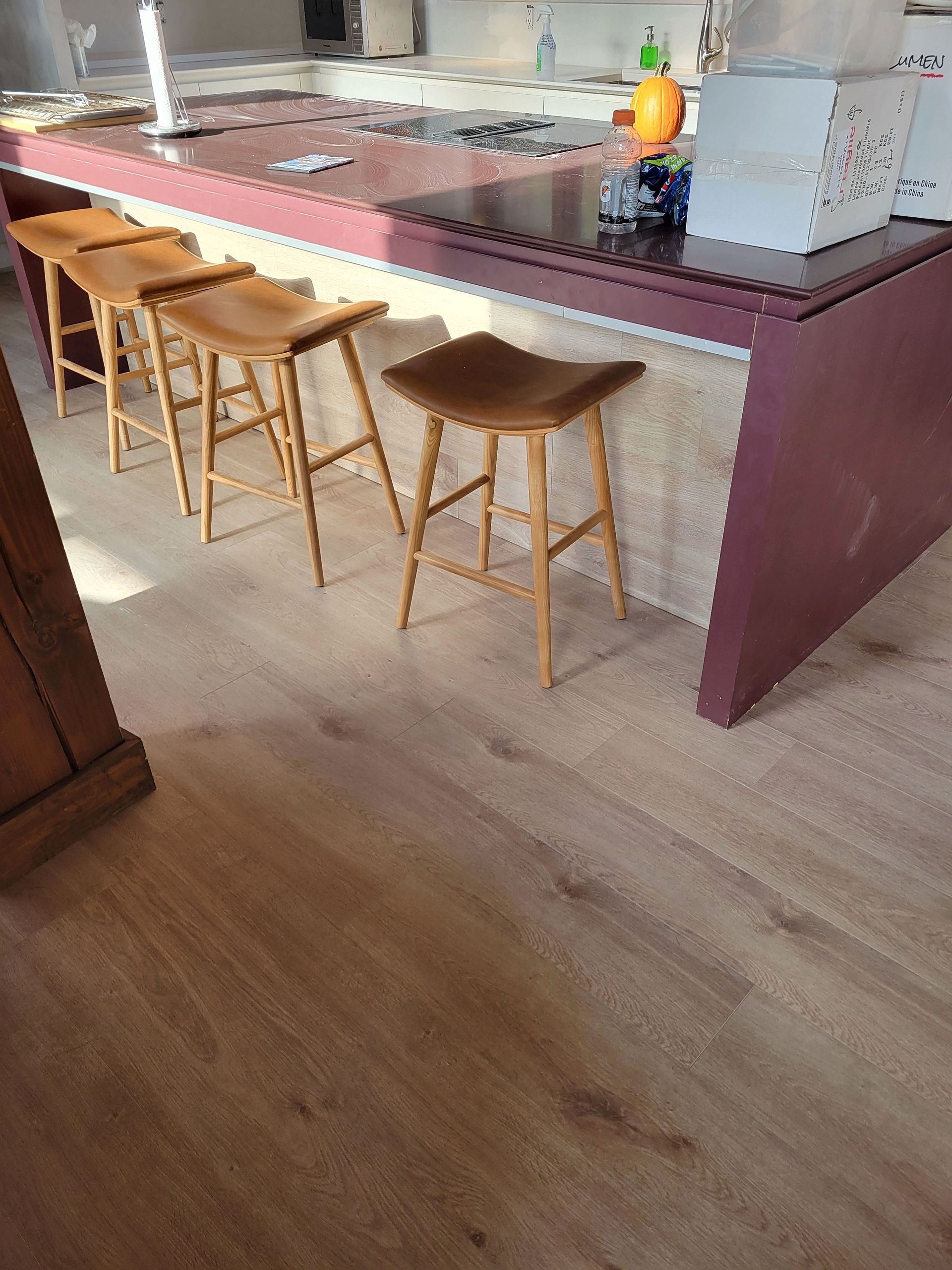 Quatre tabourets de bar en bois étaient alignés le long d'un îlot de cuisine rouge foncé avec un socle en pierre et un sol en bois clair.