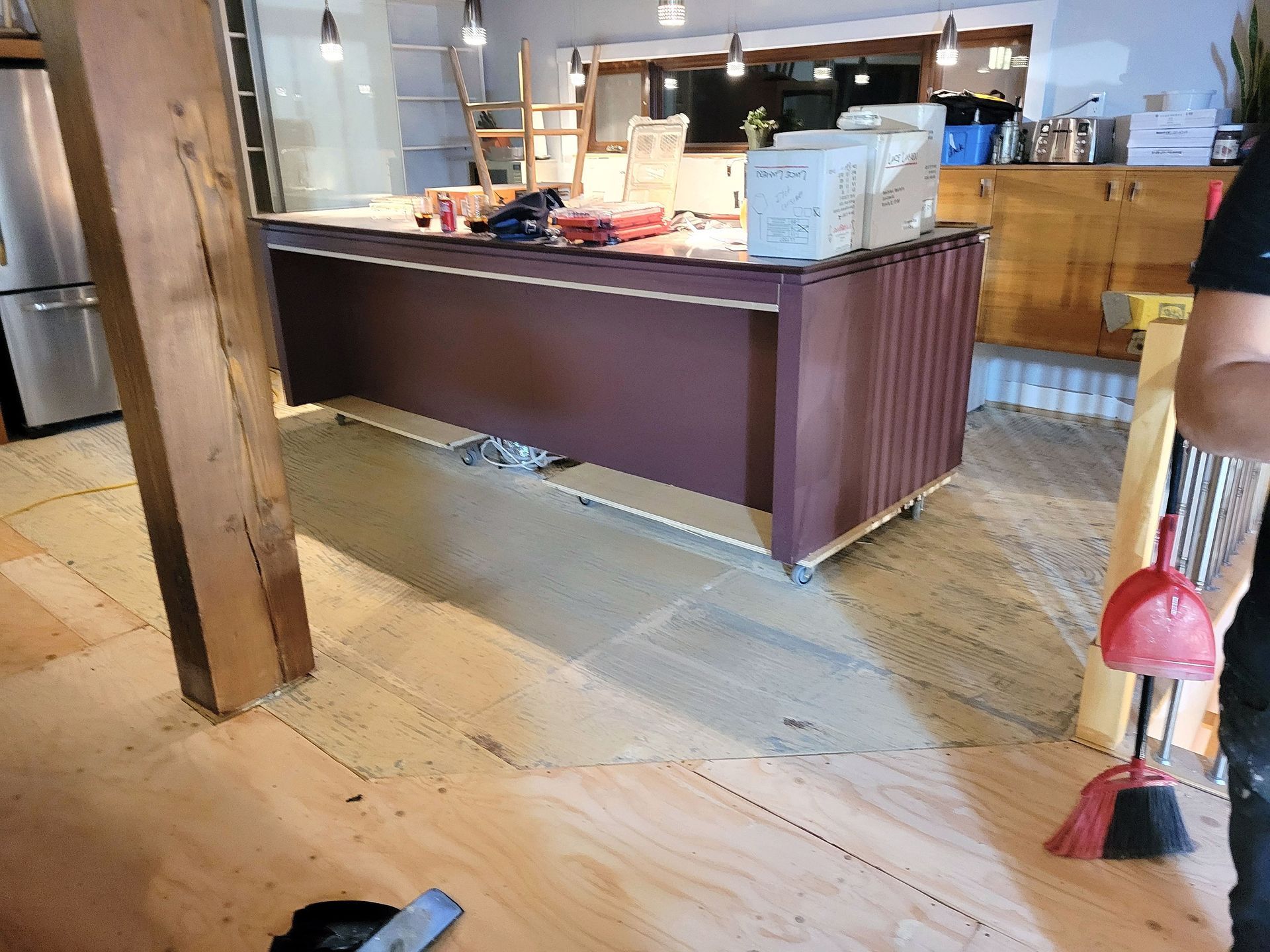 Un îlot de cuisine brun foncé trône sur un parquet à moitié fini dans une pièce en rénovation.