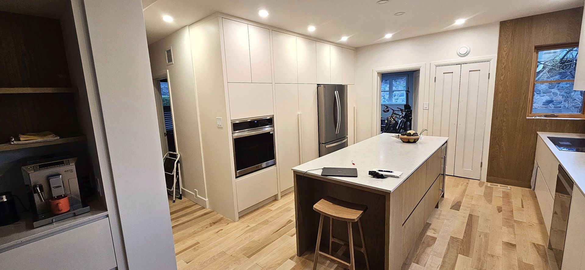 Une cuisine moderne avec un îlot central blanc, des appareils électroménagers en acier inoxydable, un parquet clair et des placards allant du sol au plafond.