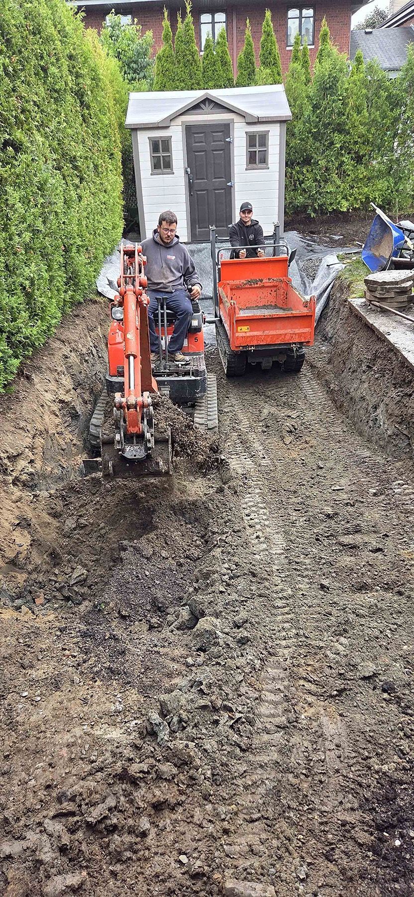 Deux personnes manœuvrent des engins de chantier orange, une pelleteuse et un tombereau, sur un terrain boueux devant un abri de jardin.