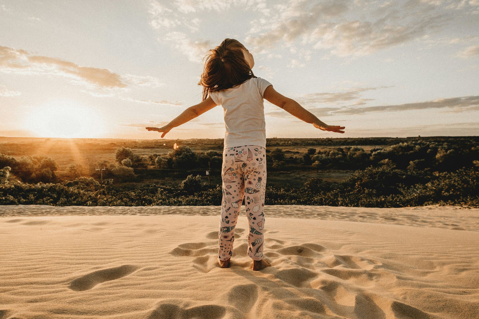 A little girl standing on top of a sand dune with her arms outstretched