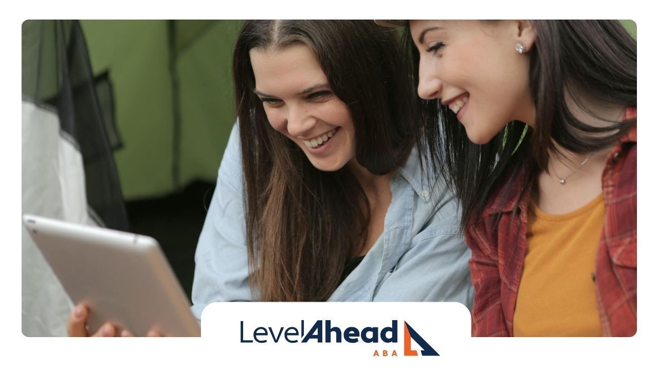 Two autistic adults laughing while looking at a tablet in a relaxed outdoor setting in Georgia.