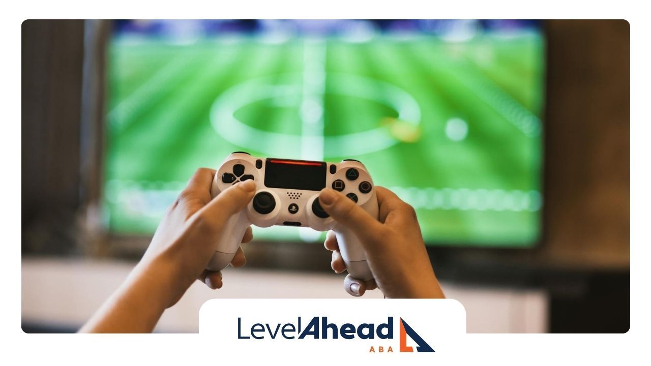 Hands of an autistic adult holding a video game controller in front of a TV showing a sports field.