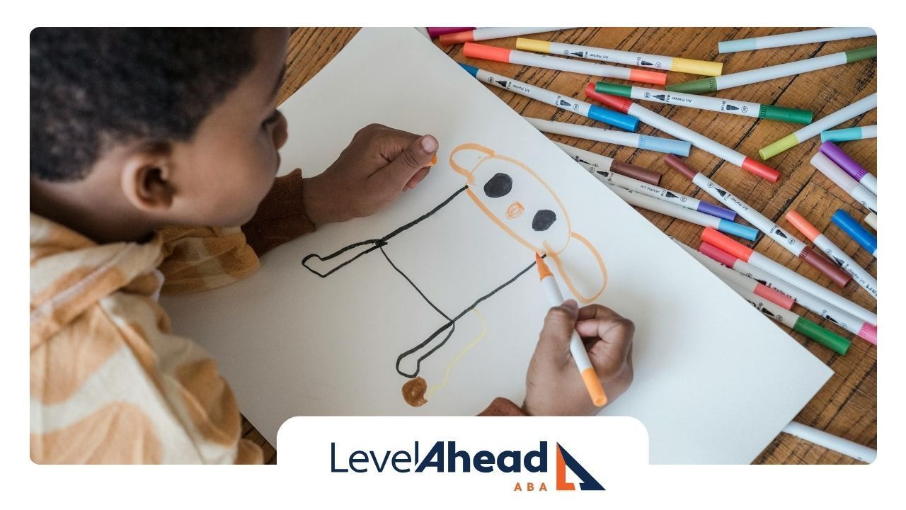 An autistic child drawing on a paper, surrounded by markers scattered across a wooden table in NE.