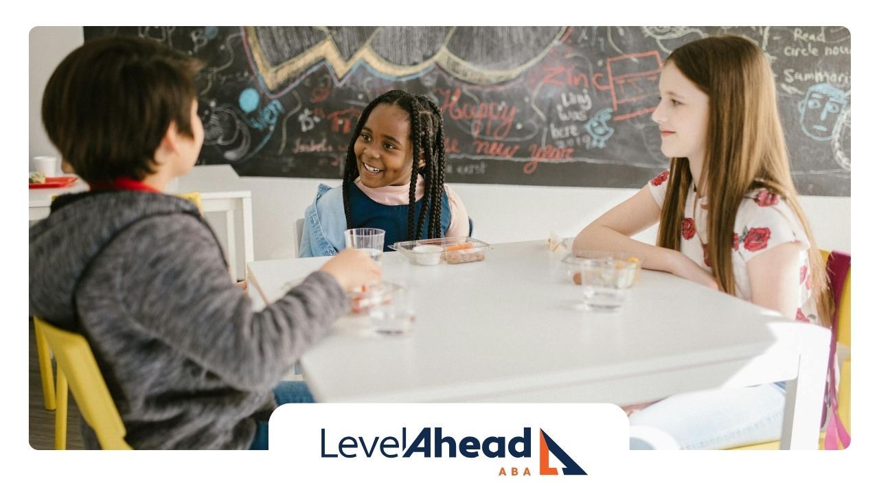 Autistic children sitting at a table, engaging in a discussion with smiles and a chalkboard in GA.