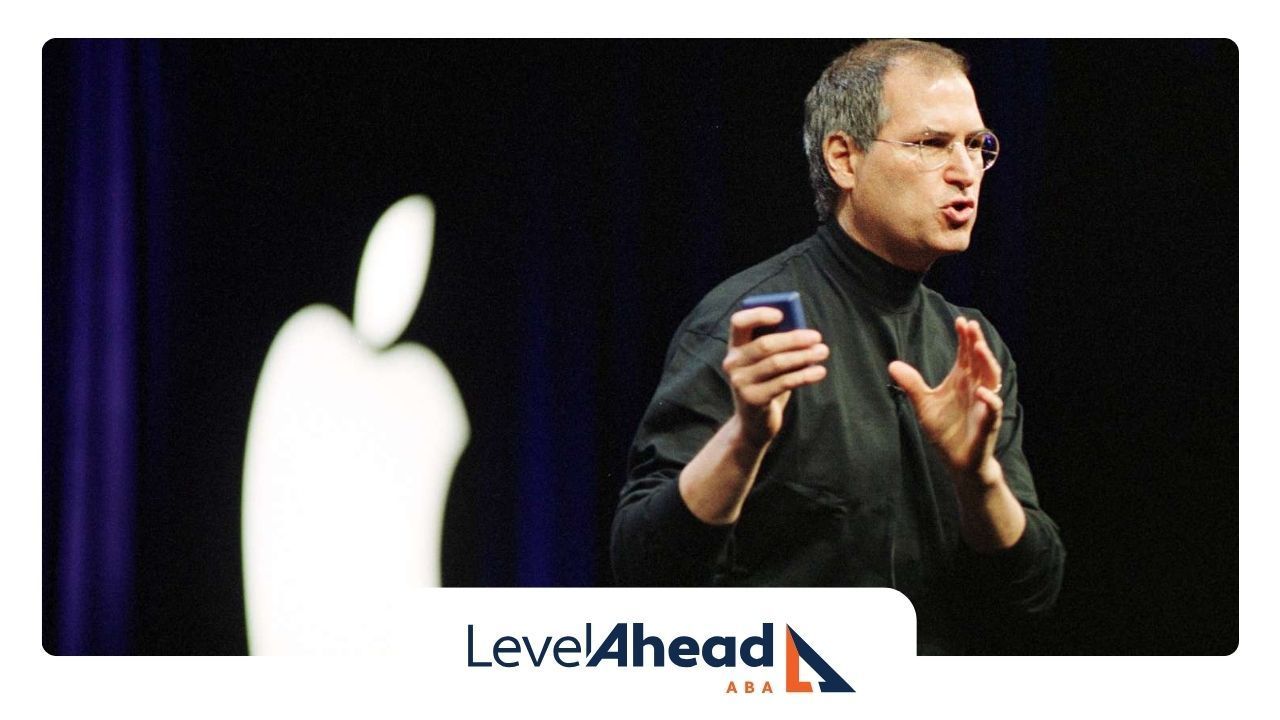 Steve Jobs on stage delivering a presentation, with an Apple logo displayed in the background.