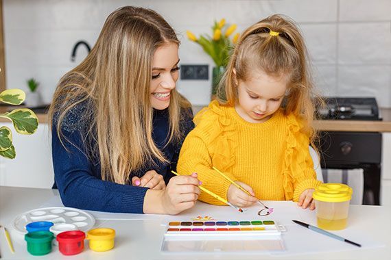 A woman and a little girl sitting at a table painting with watercolors 