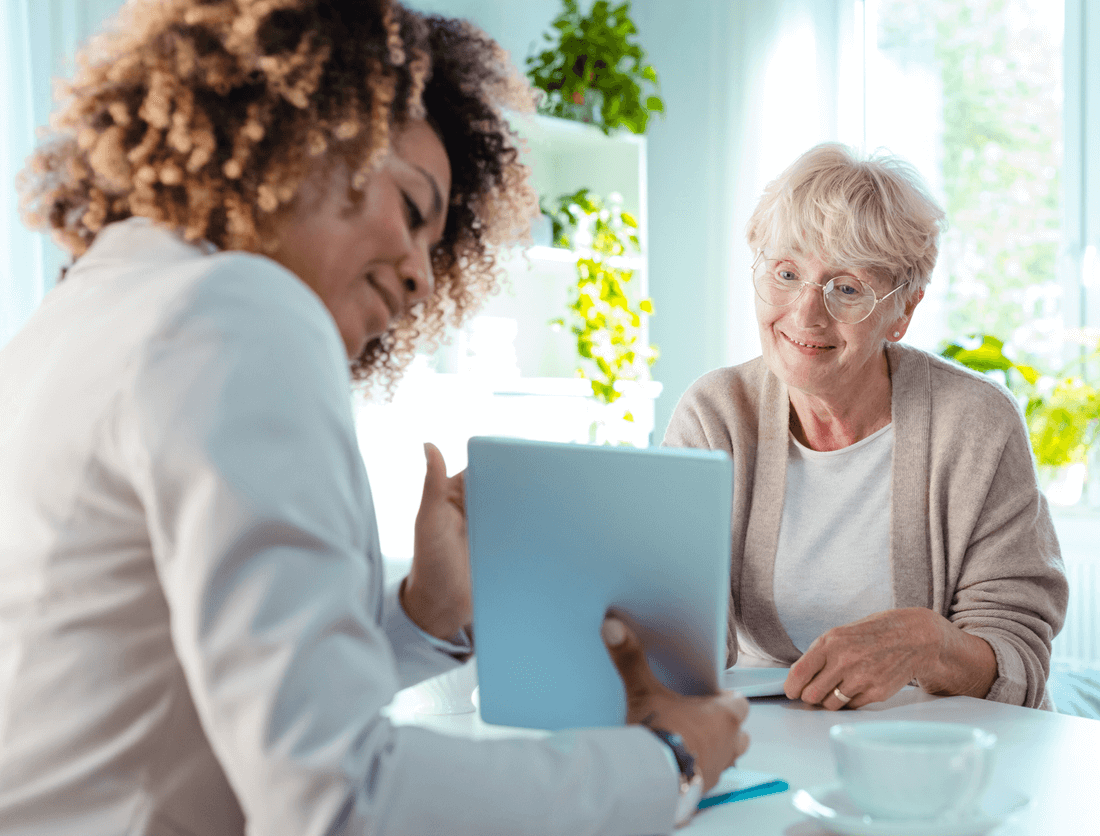 A woman is standing next to an elderly woman in a hospital bed.