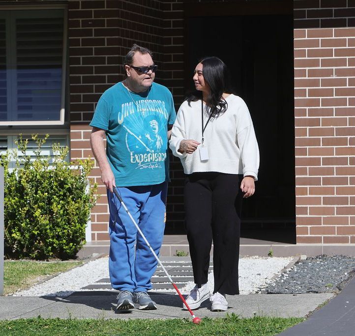 A man and a woman are walking down a sidewalk in front of a brick house