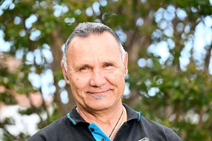 A man in a black and blue polo shirt is smiling for the camera.