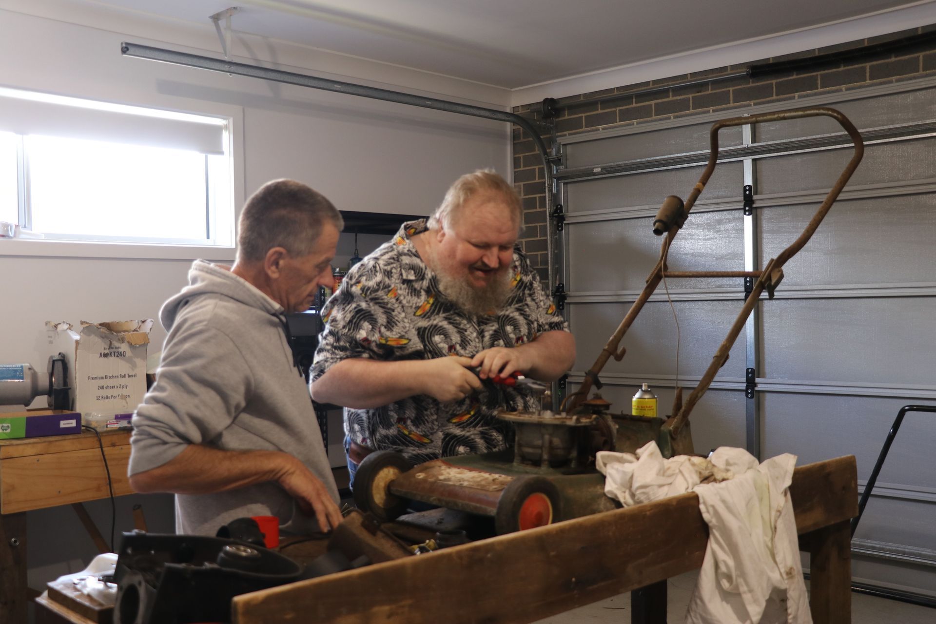 Two men are working on a lawn mower in a garage.