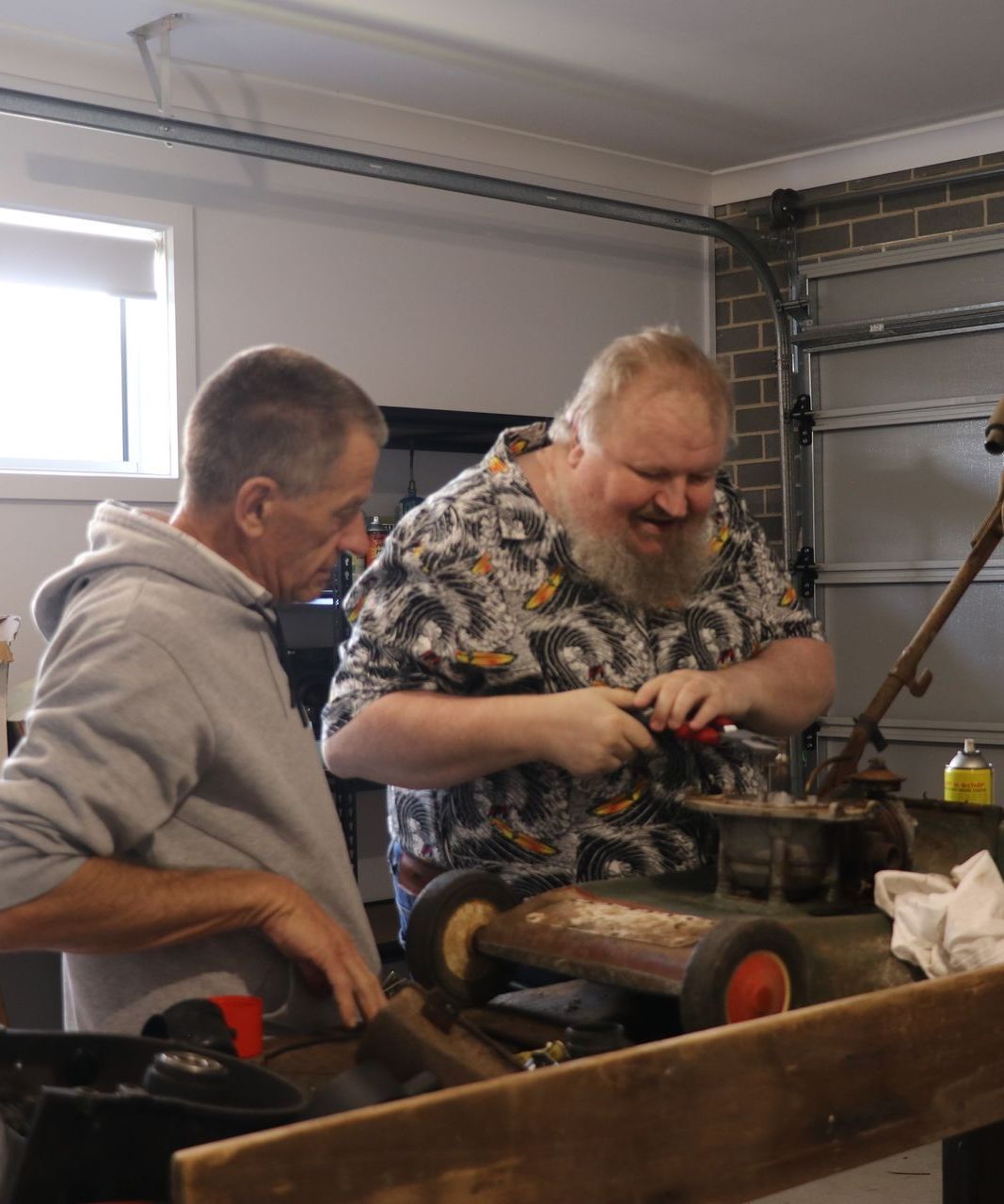 Two men are working on a lawn mower in a garage