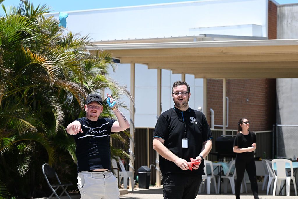 Two men are standing in front of a building holding remote controls.