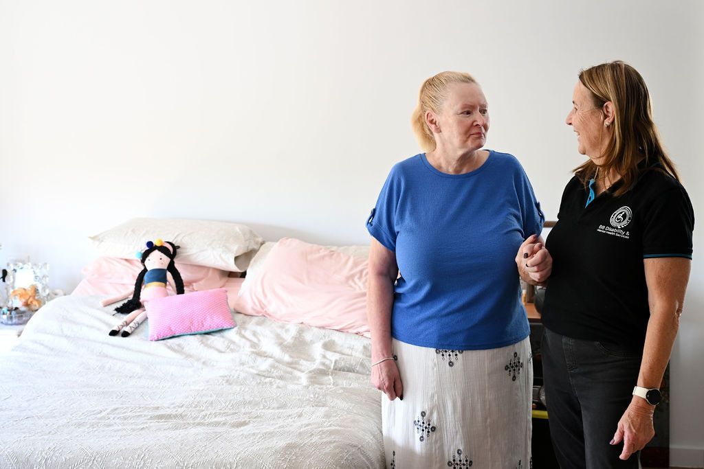 Two women are standing next to each other in front of a bed.