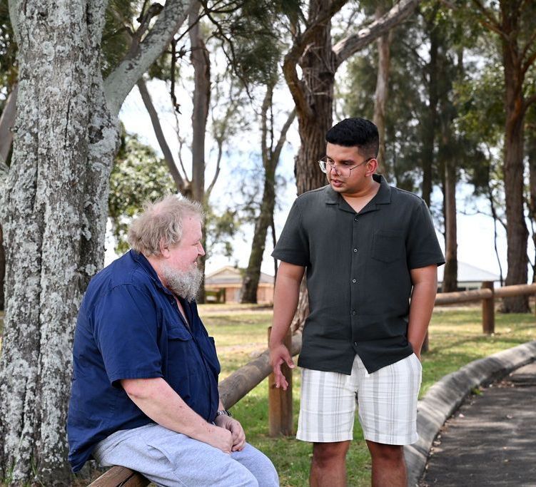 Two men are sitting under a tree talking to each other