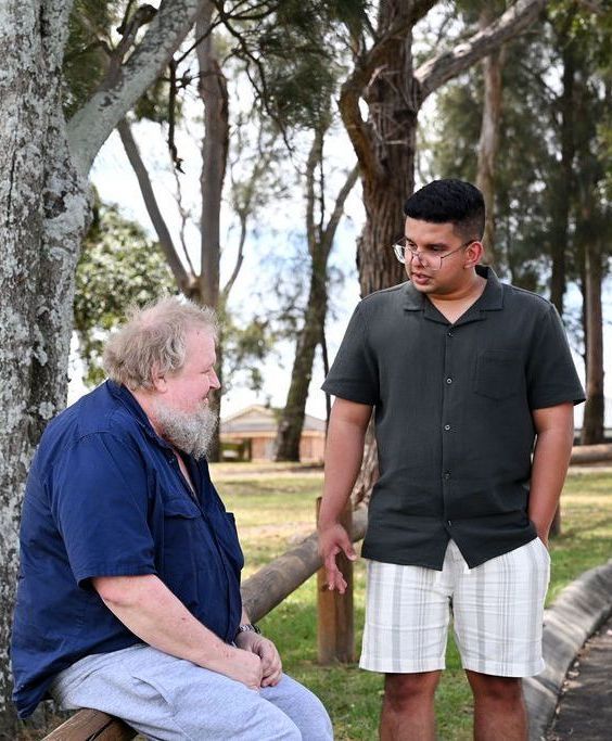 Two men are standing next to each other in a park talking to each other.