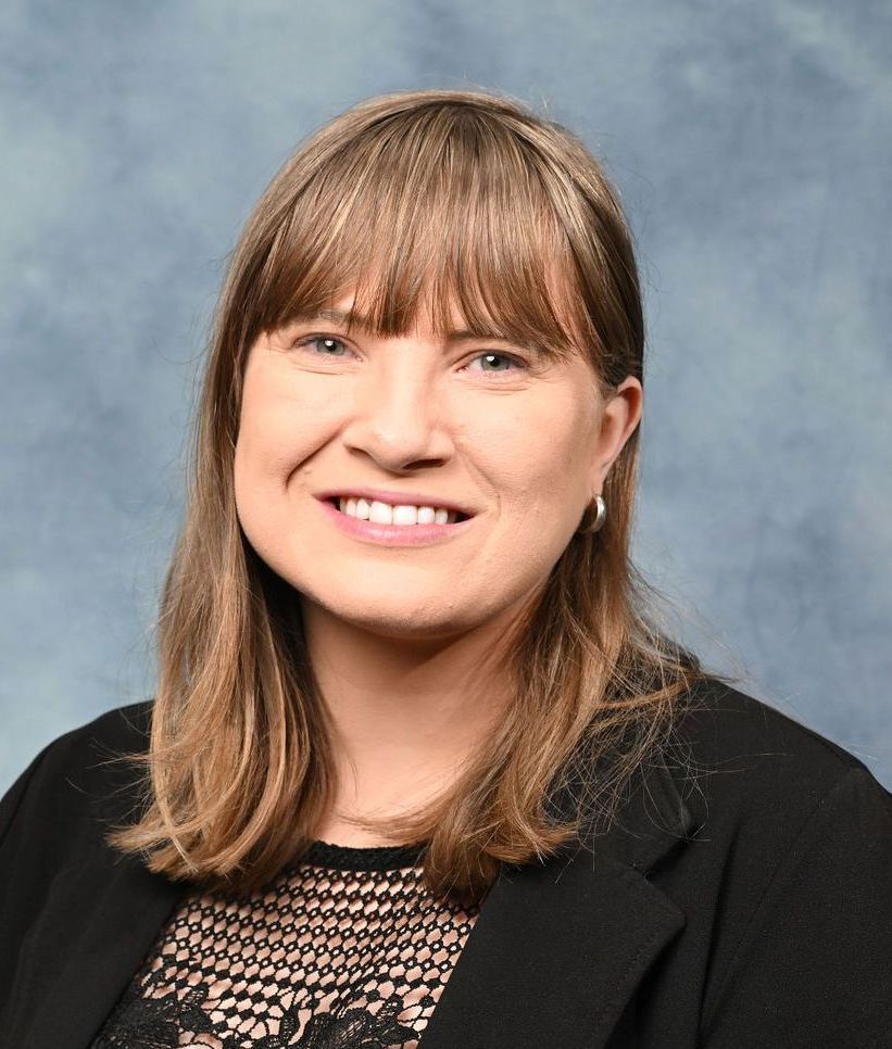 A woman in a black jacket is smiling for the camera.