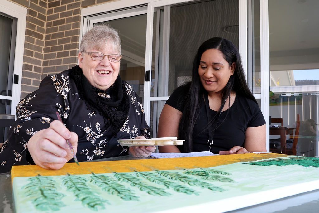 Two women are sitting at a table painting a picture.