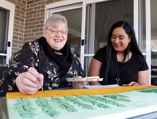 Two women are sitting at a table painting a picture.