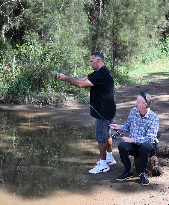 Two men are standing next to each other in a park talking to each other.