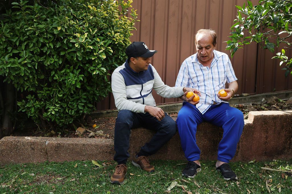 Two men are sitting in the grass eating oranges