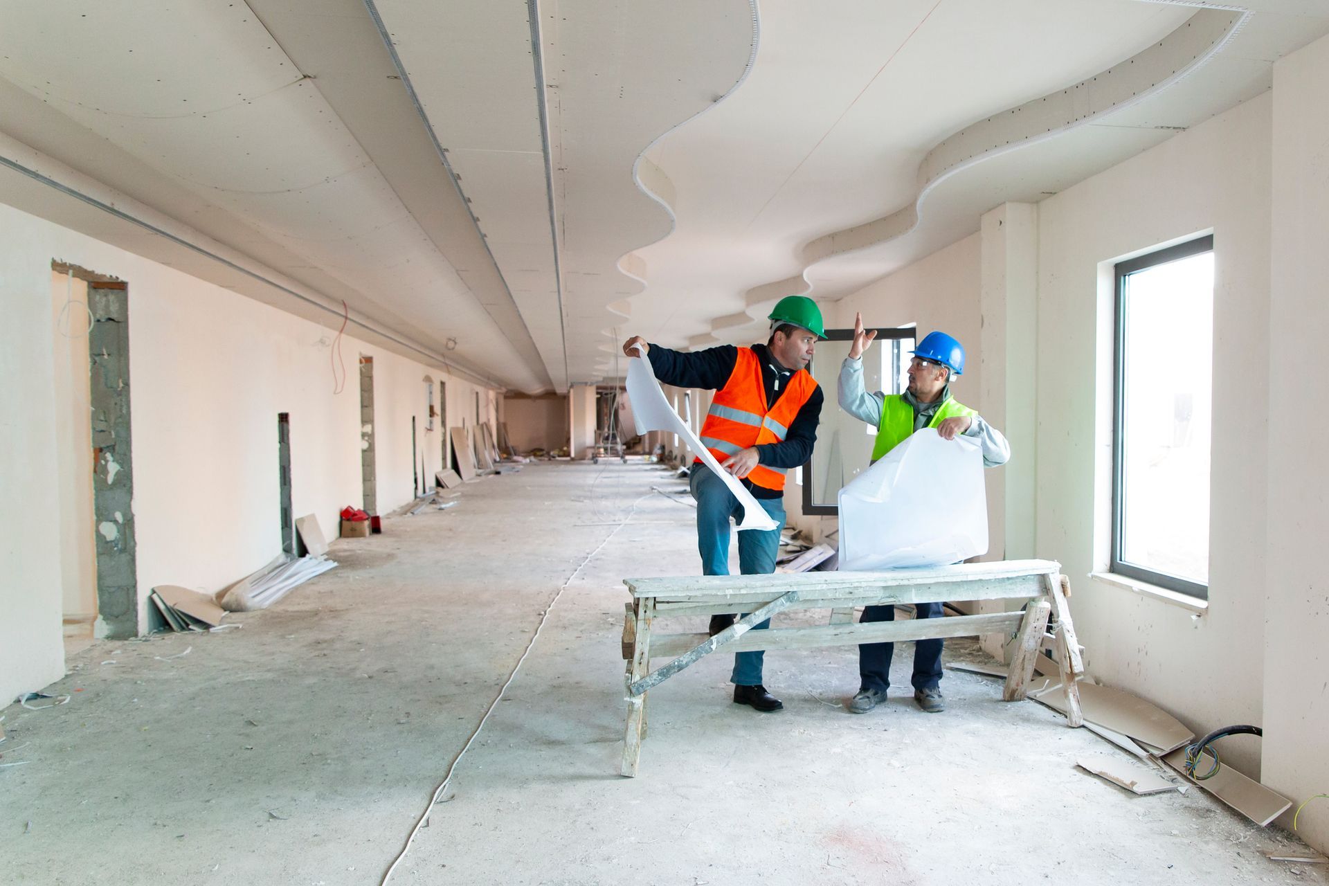 Two construction workers are looking at blueprints in an empty room.