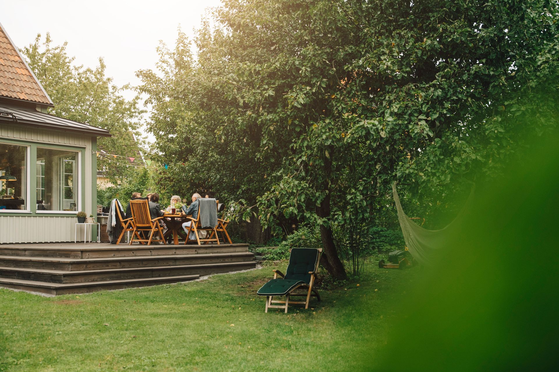 A group of people are sitting at a table in the backyard of a house.