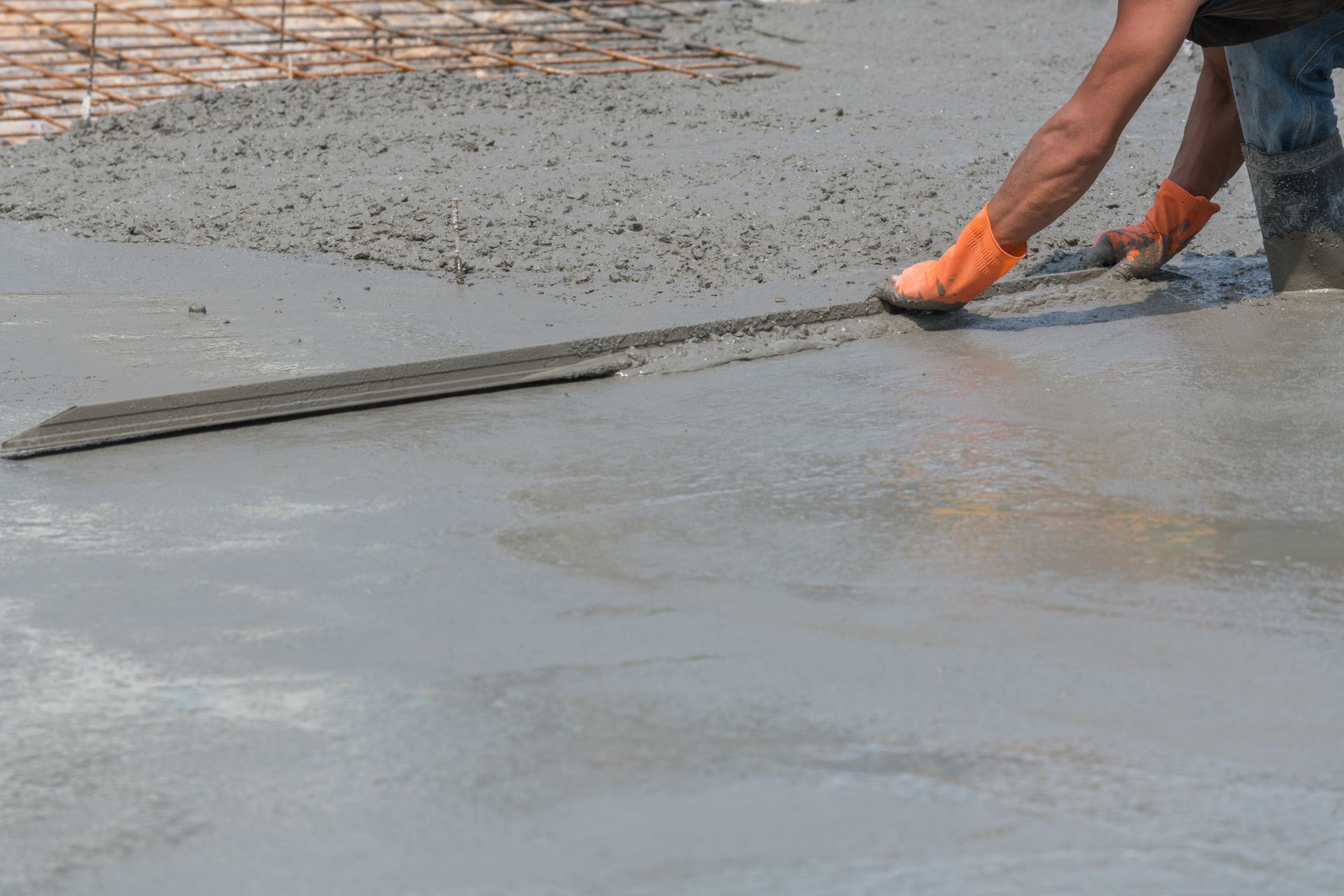 A man is spreading concrete on the ground with a trowel.