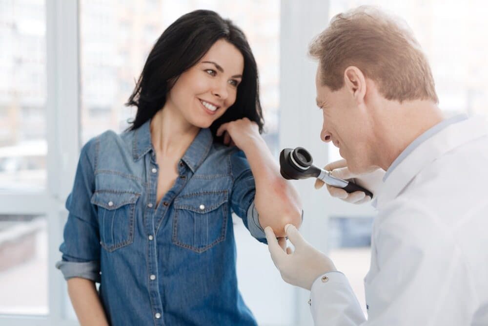 A Doctor Is Examining A Woman 's Elbow With A Magnifying Glass — Health Hub Mackay In North Mackay, QLD