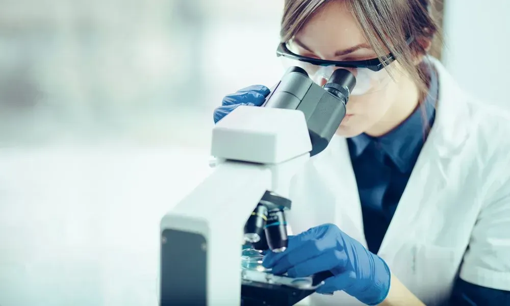 A Woman Is Looking Through A Microscope In A Laboratory — Health Hub Mackay in Mackay, QLD