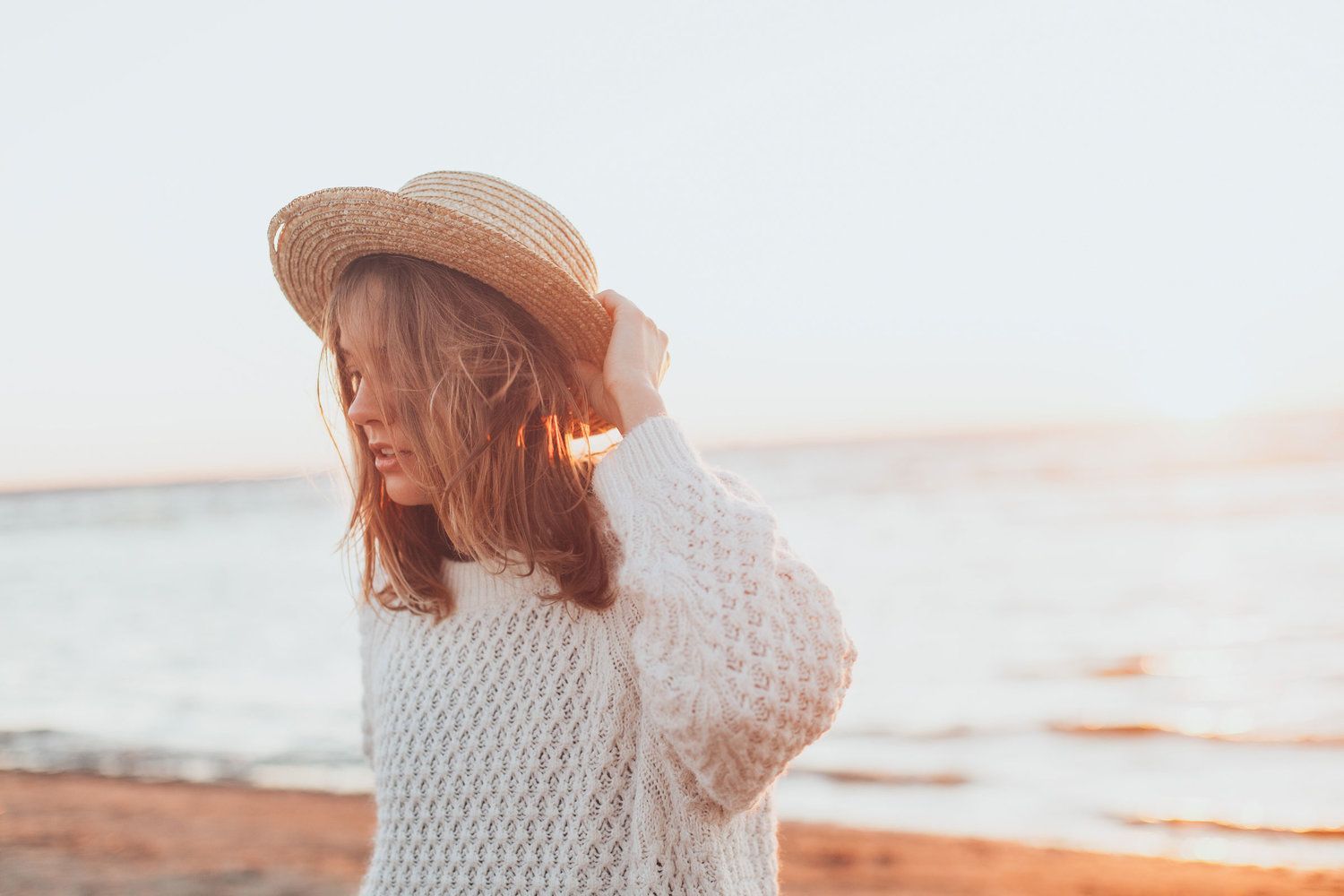 A Woman Wearing A Straw Hat And A White Sweater Is Standing On The Beach — Health Hub Mackay in Mackay, QLD