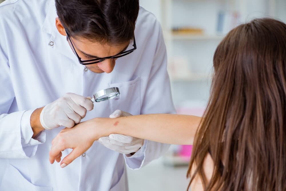 A Doctor Is Examining A Woman 's Arm With A Magnifying Glass — Health Hub Mackay In North Mackay, QLD
