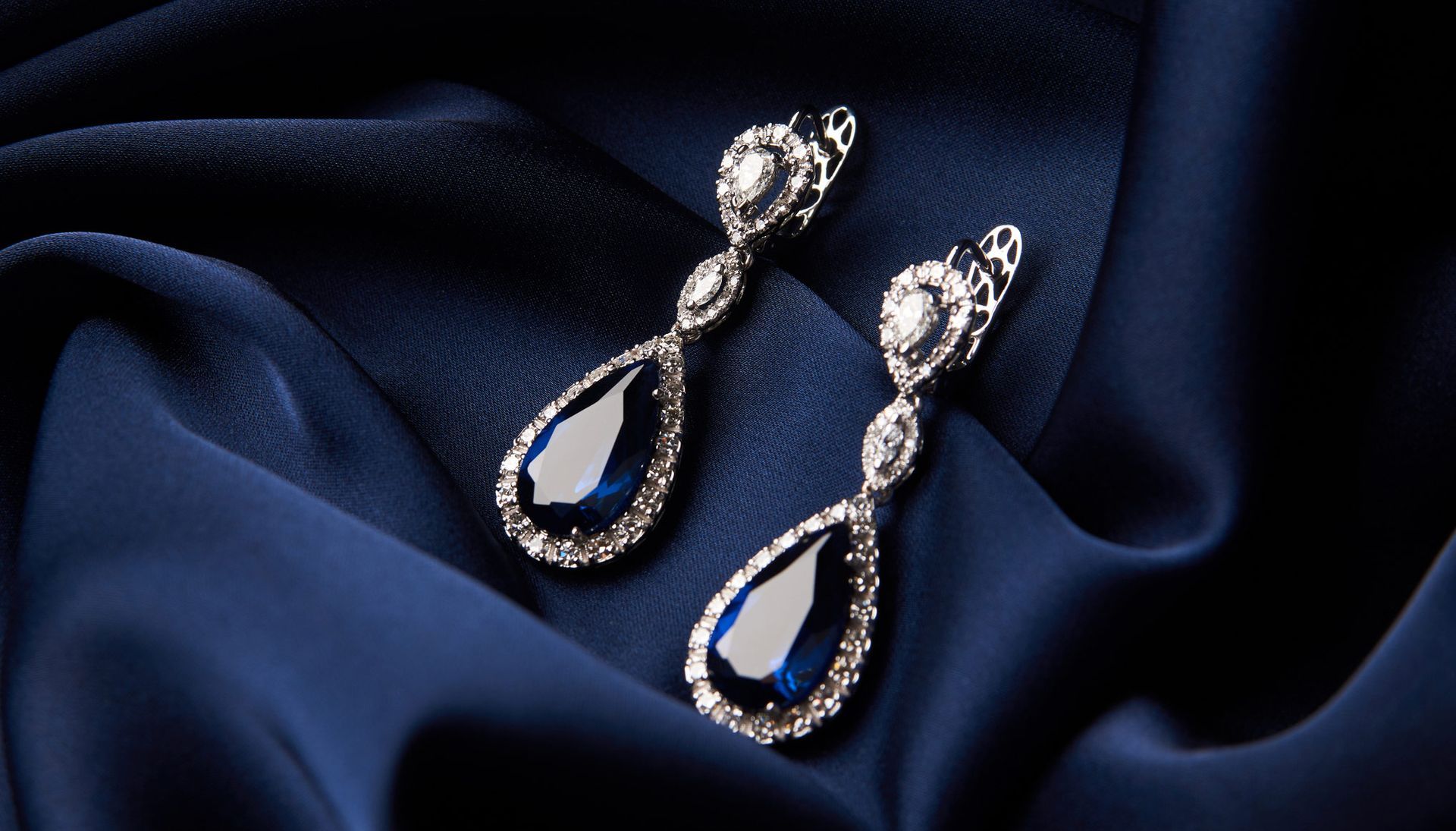 Pair of sapphire and diamond drop earrings on navy blue silk.