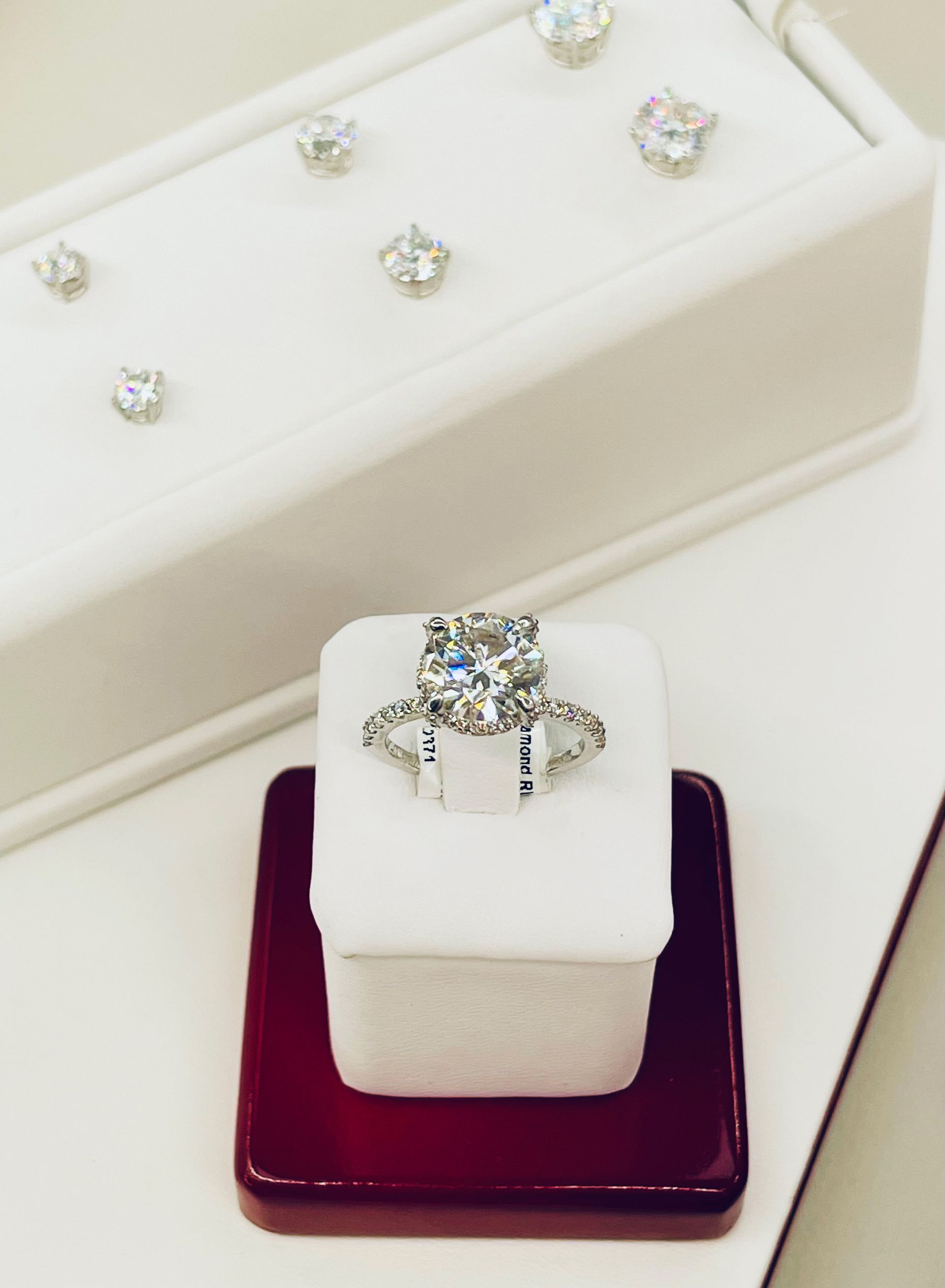 Diamond ring on white display, with additional diamonds in the background.