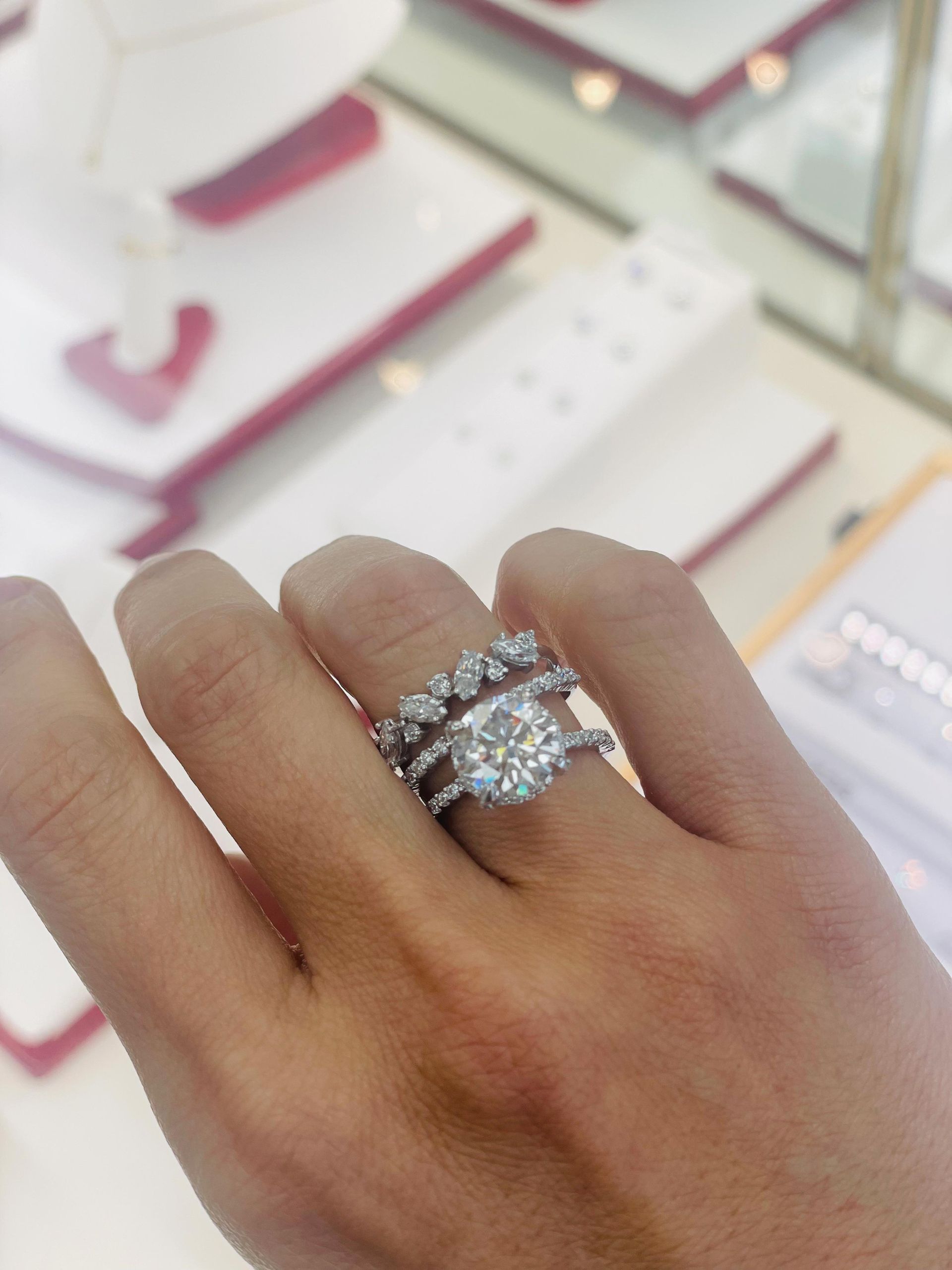 Hand wearing three diamond rings in a jewelry store setting.