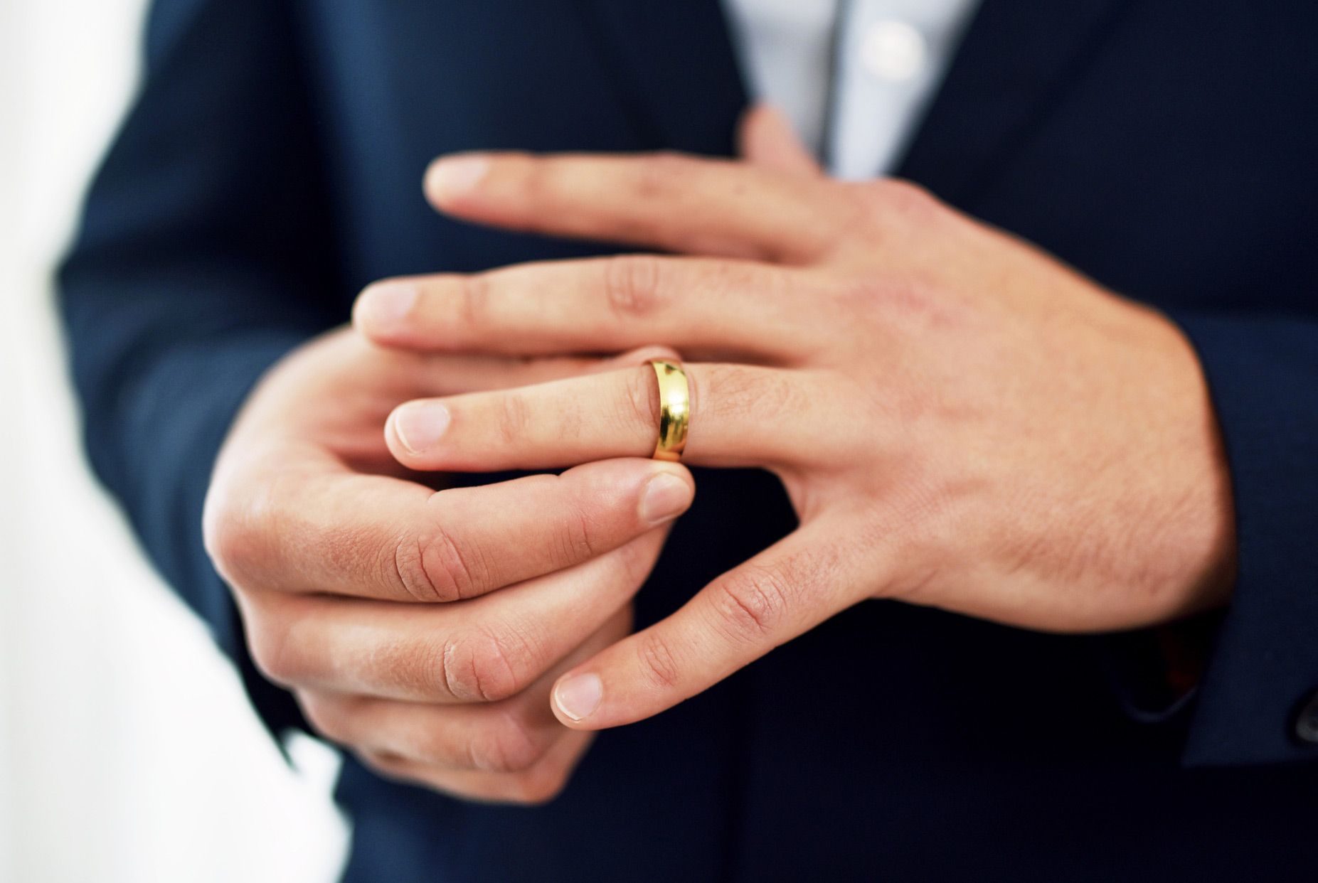 Man in a suit adjusting a gold wedding ring on his finger.
