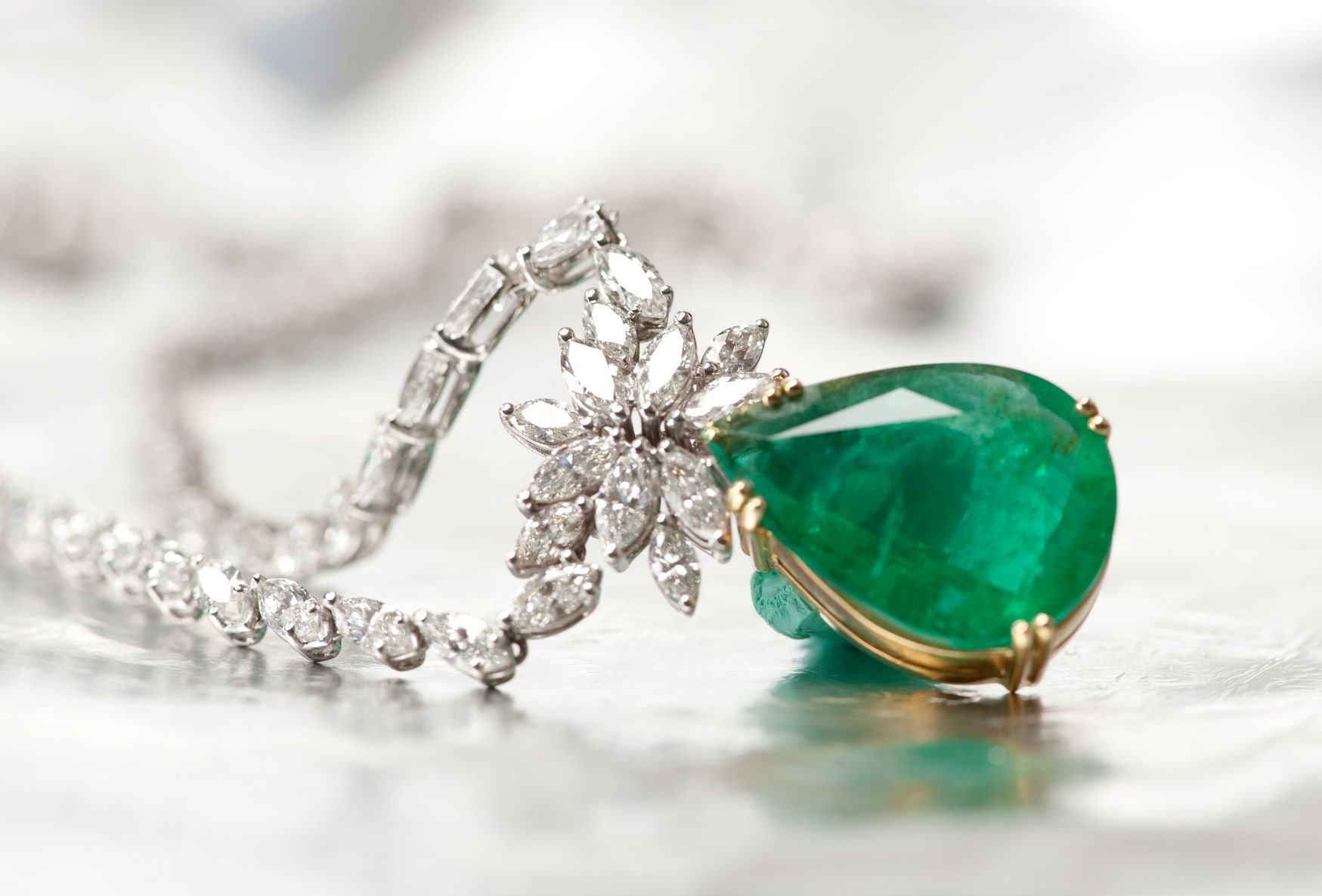 Emerald pendant necklace with diamonds on a reflective surface.