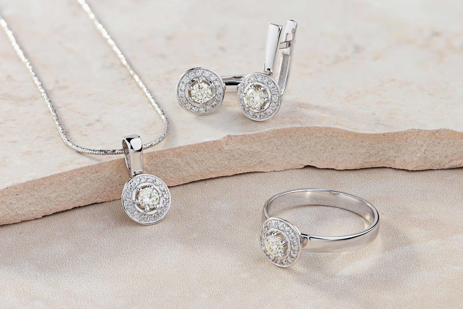Silver jewelry set: necklace, earrings, and ring, each with a central diamond surrounded by smaller stones.