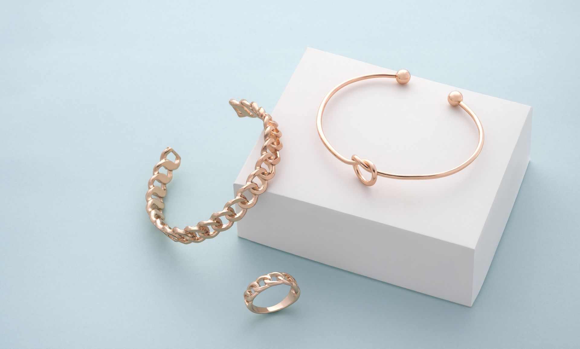 Gold bracelets and ring on white block, light blue backdrop.