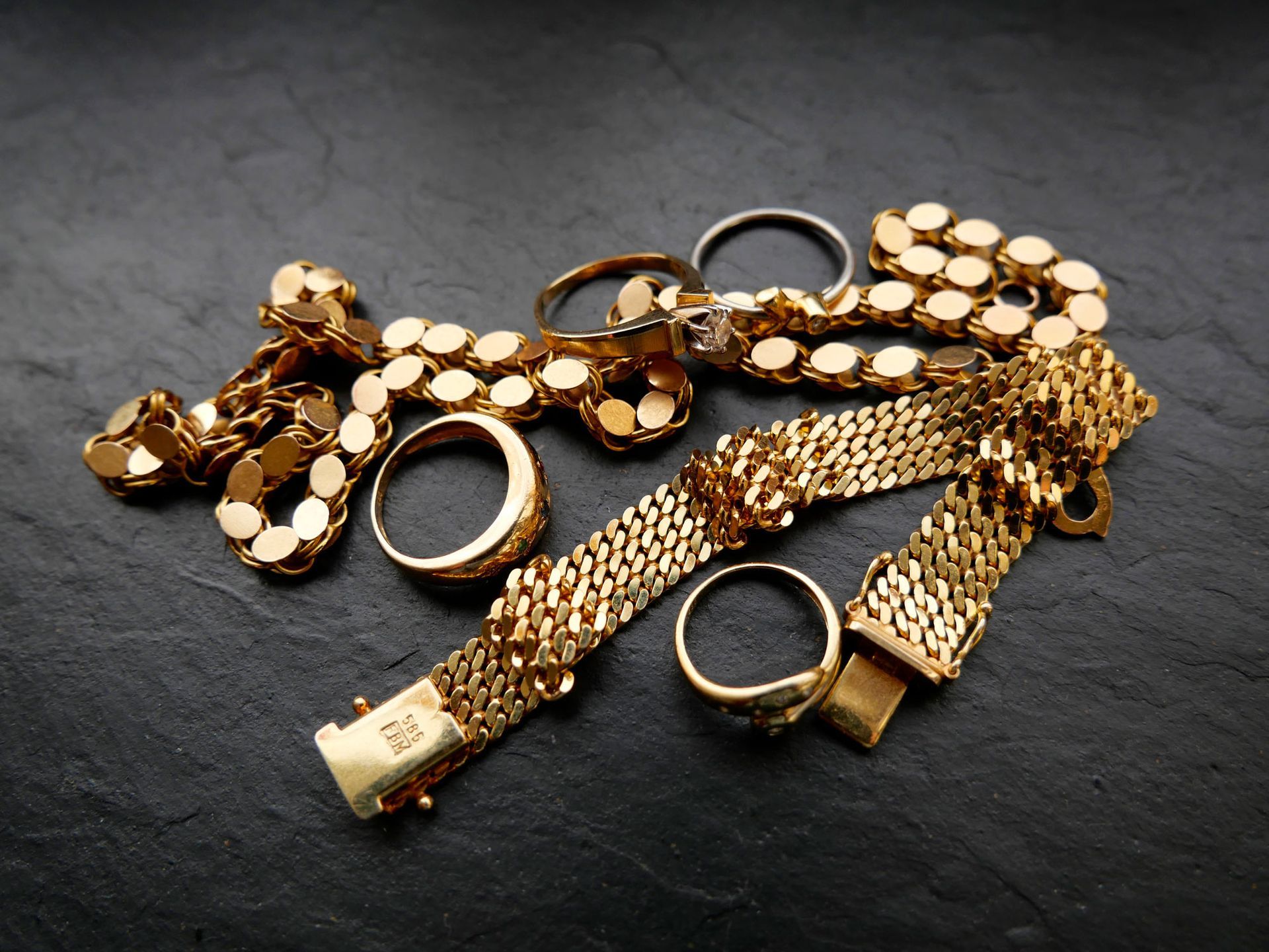 Gold jewelry on dark stone surface: rings and bracelets.
