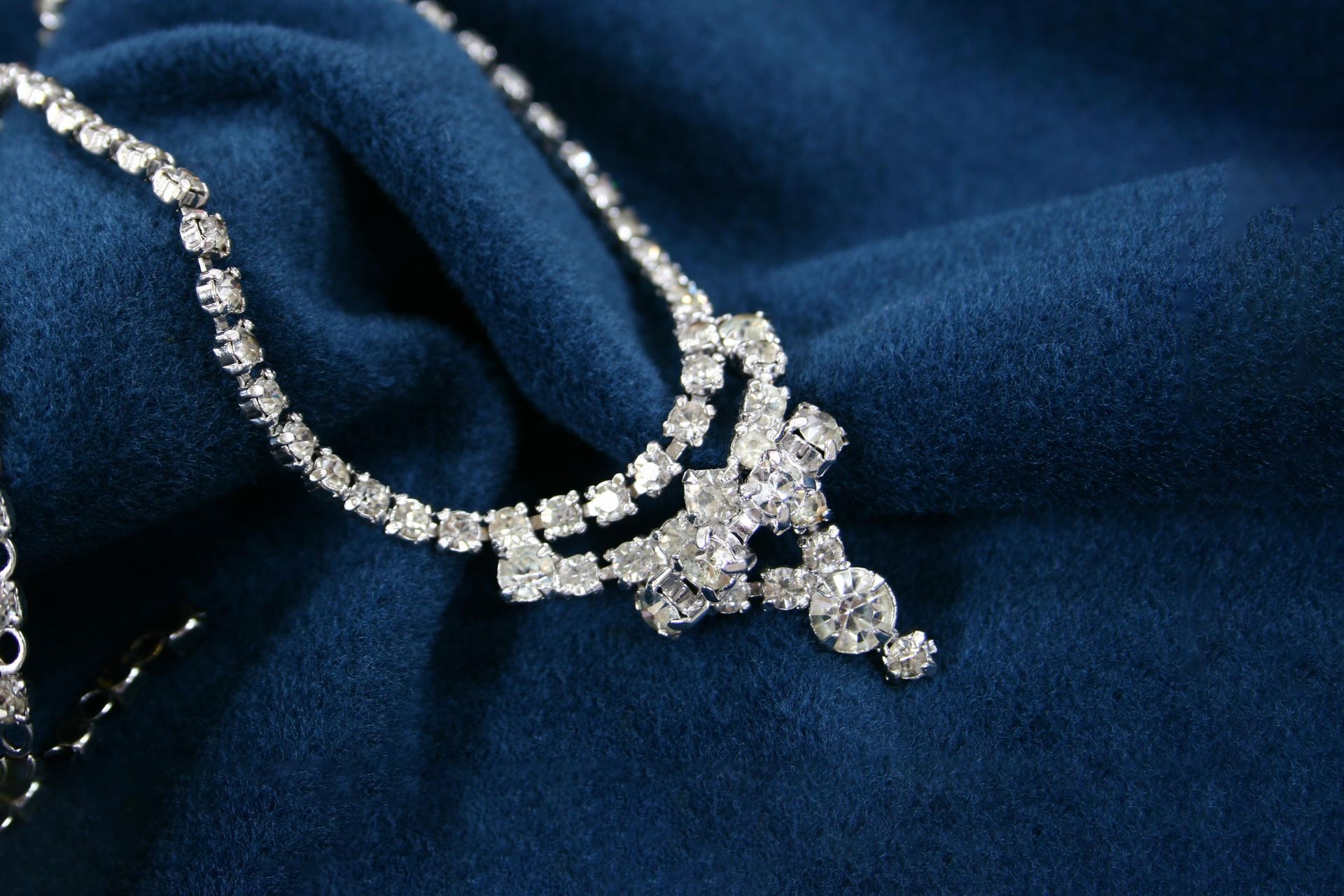 Silver rhinestone necklace on a dark blue fabric.