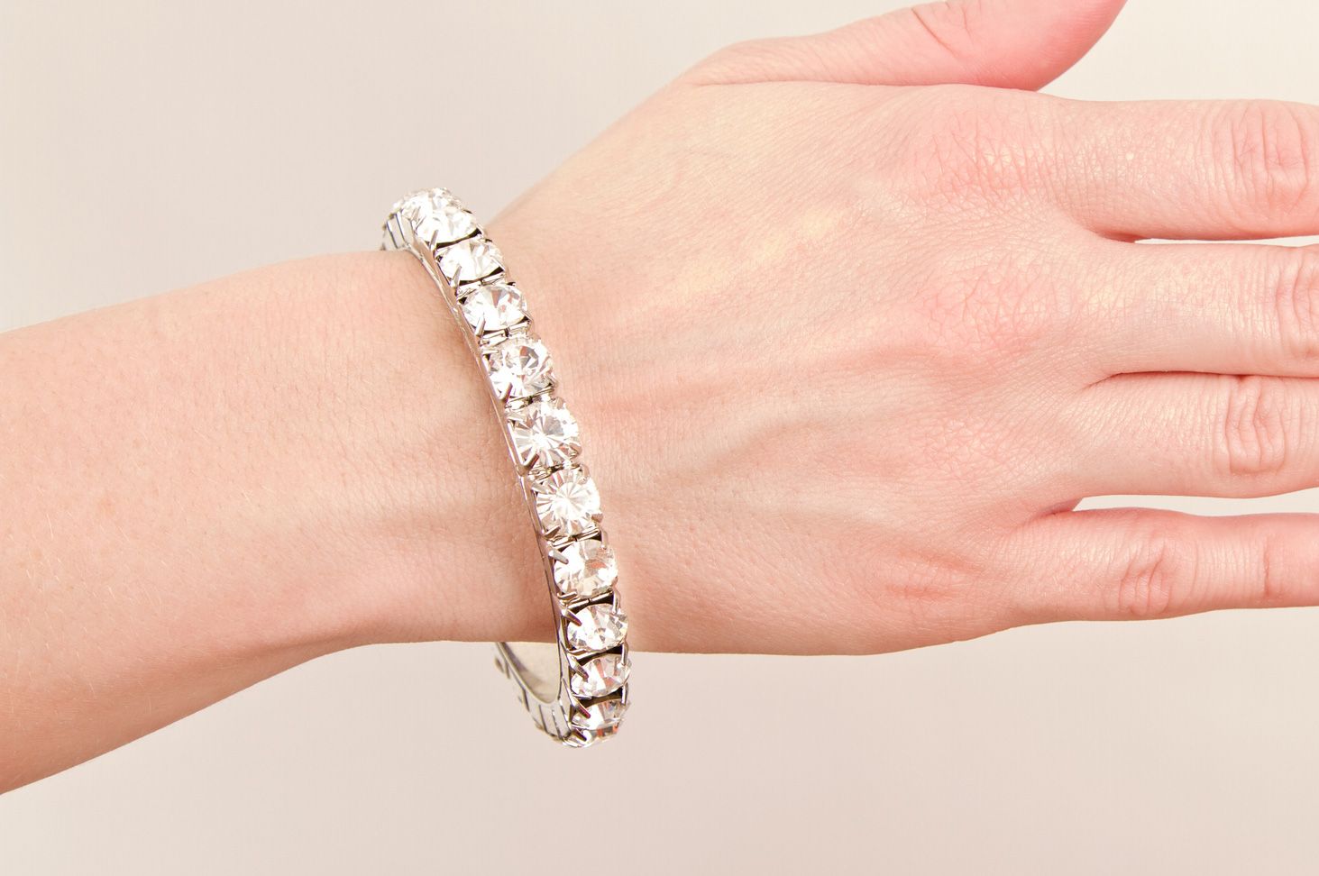 Person's wrist wearing a sparkly bracelet made of clear gems on a light background.