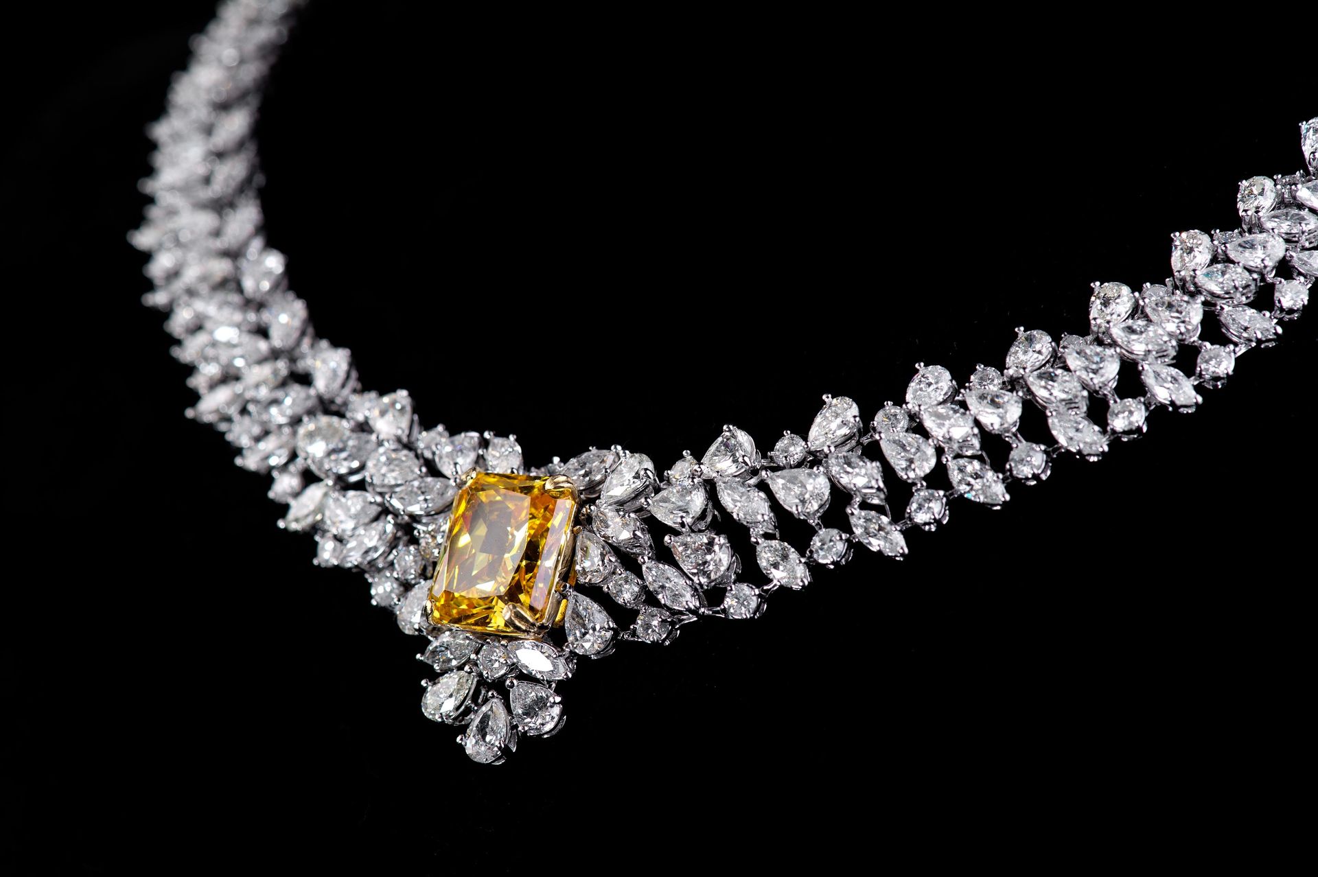 Diamond necklace with a yellow center stone, sparkling against a black background.
