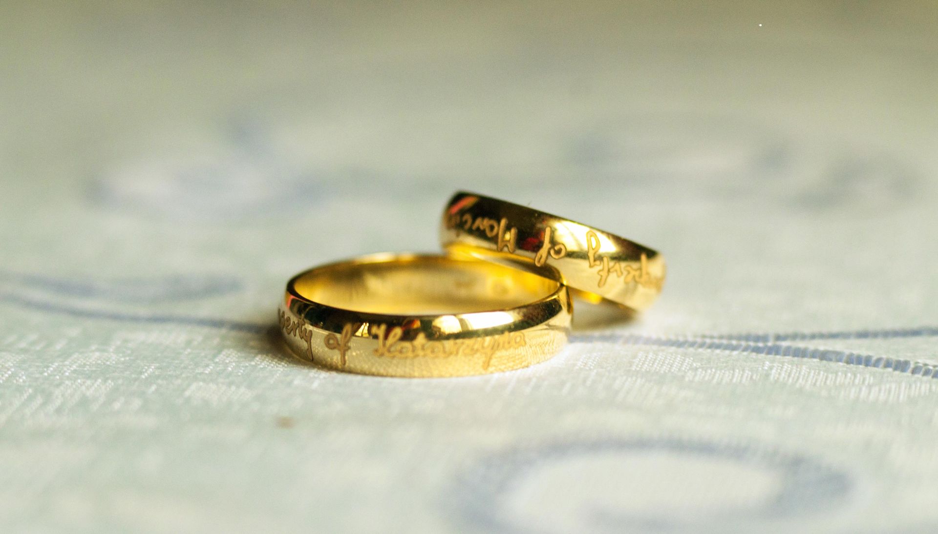 Two gold wedding rings stacked on top of each other; inscribed with text on a patterned surface.