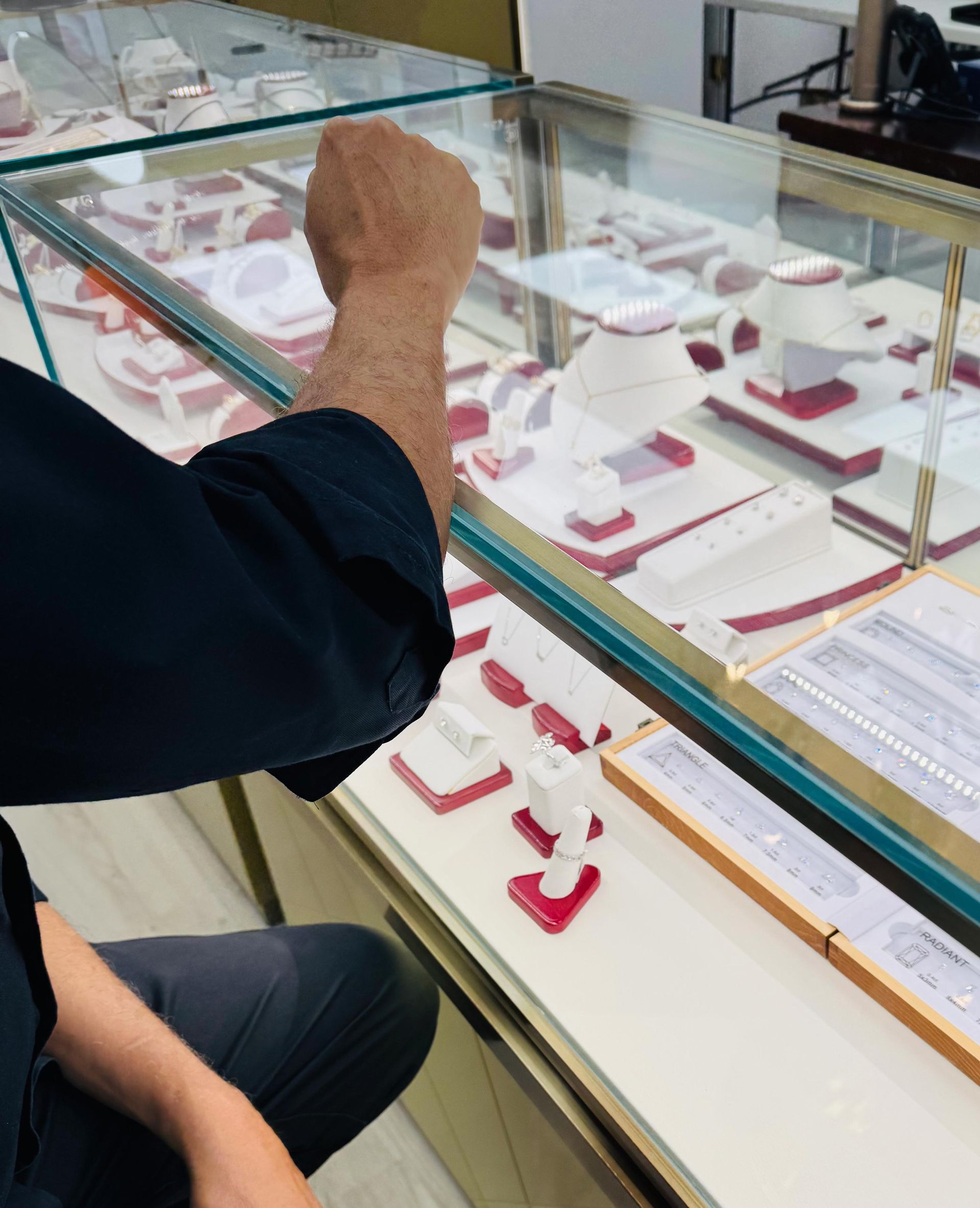 Person looking at jewelry in a display case. They are wearing dark clothing in a jewelry store.