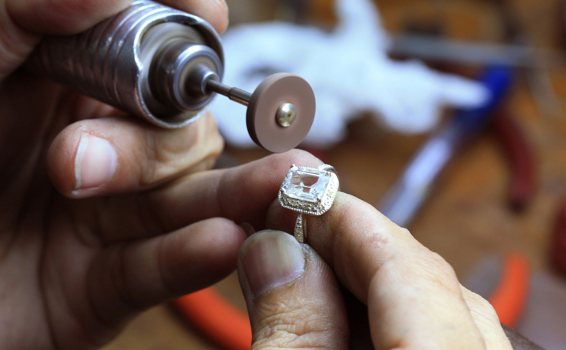 Jeweler using a rotary tool to polish a diamond ring, close-up on hands and ring.